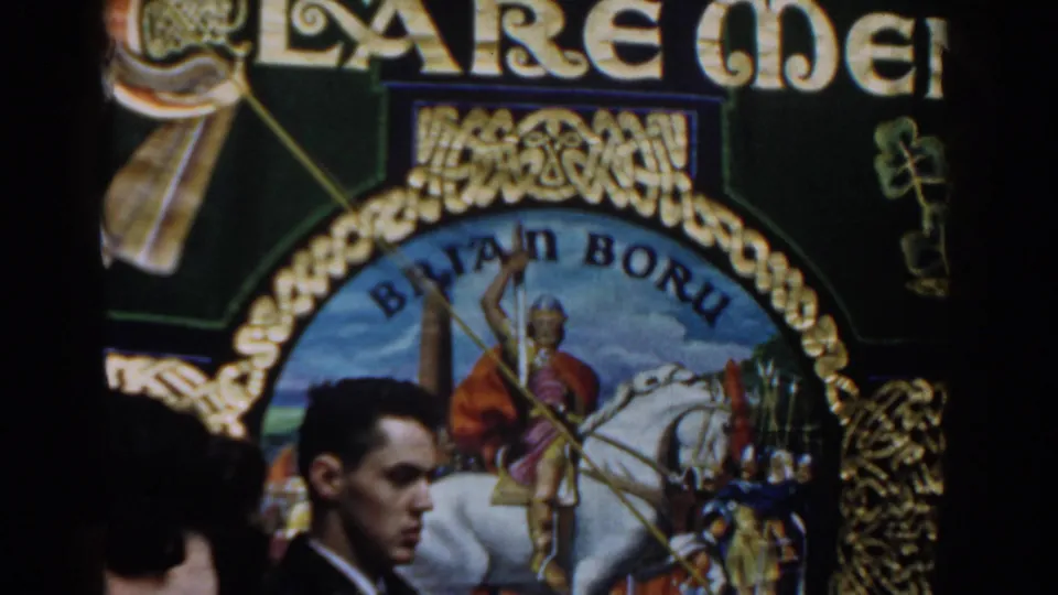 Close street-side view of a decorated parade banner with visible lettering and a painted rider, partly blocked by spectators.