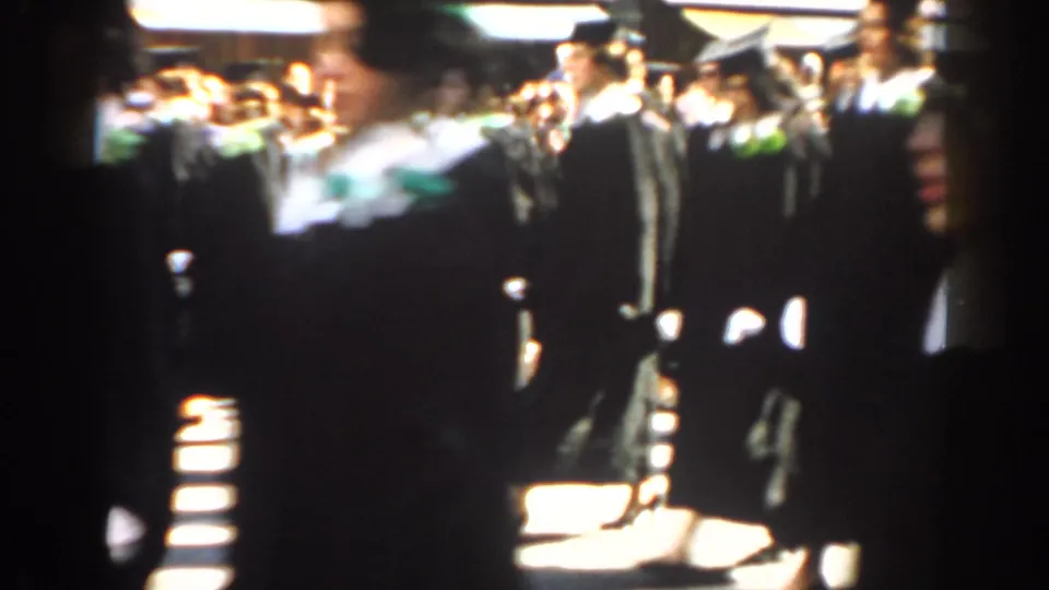 A close handheld view shows black-robed graduates passing near the camera during the 1962 New York City parade.