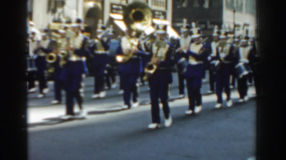 1962 New York City street-parade view with uniformed musicians, a prominent tuba, and brass players moving past storefronts.
