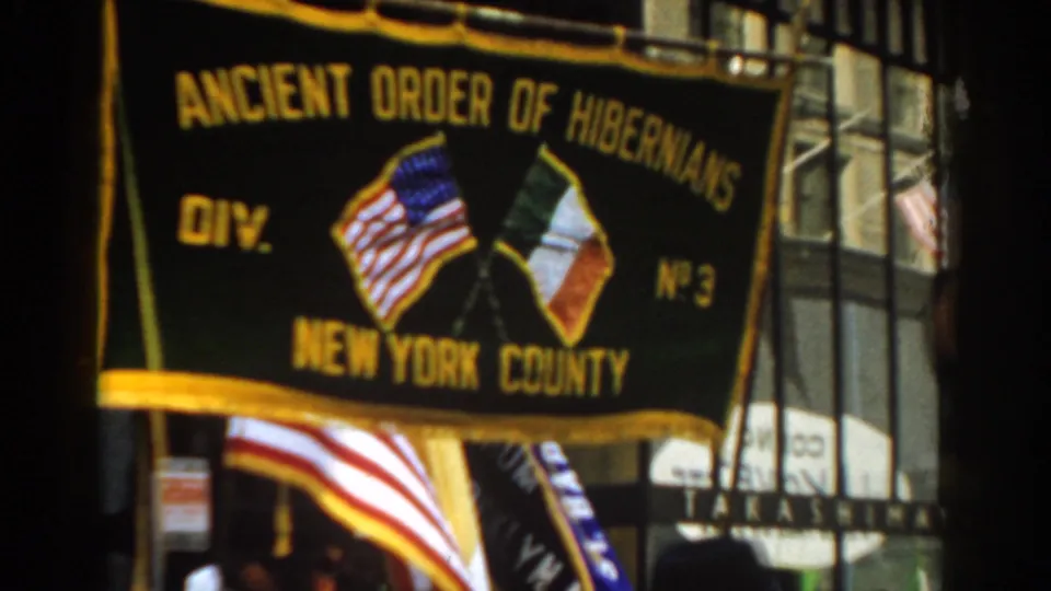 Close 1962 New York City parade view of the Ancient Order of Hibernians banner, crossed flags emblem, and American flag below.