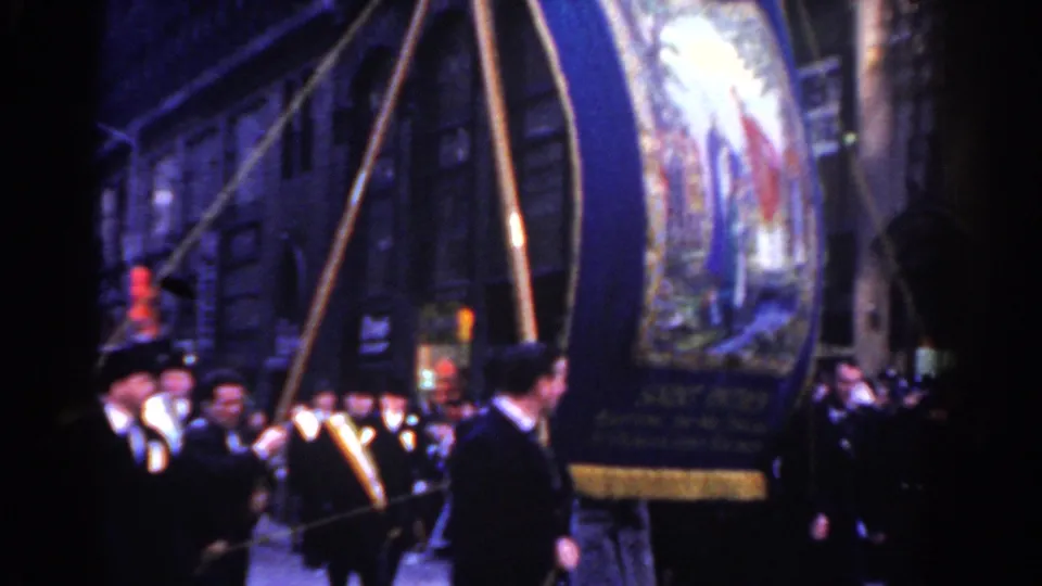 A Roscommon Society banner with religious imagery passes the camera as brass musicians and suited marchers continue the New York City parade.