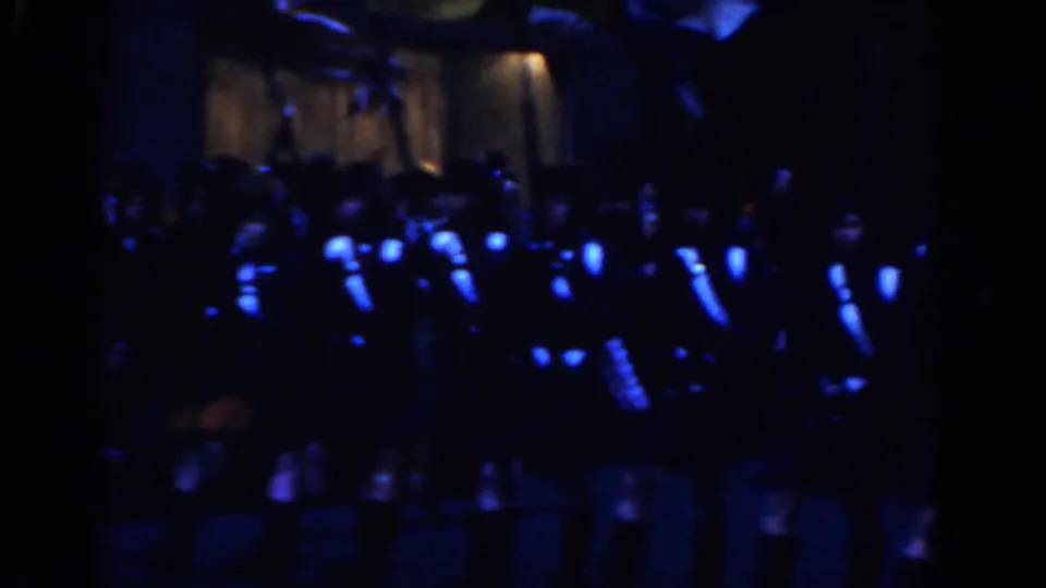 Low-light 8mm frame of a kilted marching band grouped before spectators during a 1962 New York City parade.