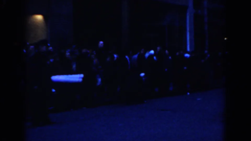 Final low-light frame showing spectators and parade performers receding along a dark New York City street.