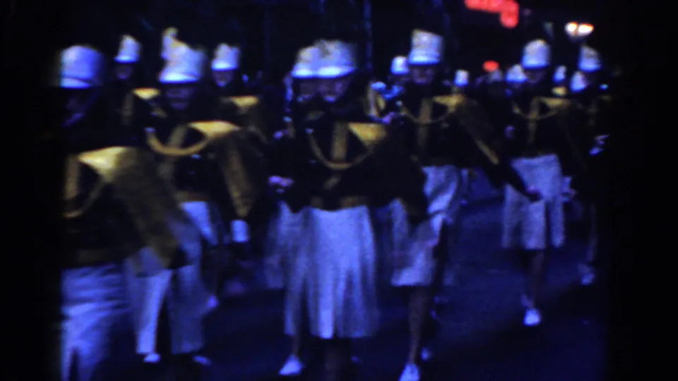 1962 New York City home-movie frame with band members approaching in coordinated white caps, gold jackets, and white skirts.