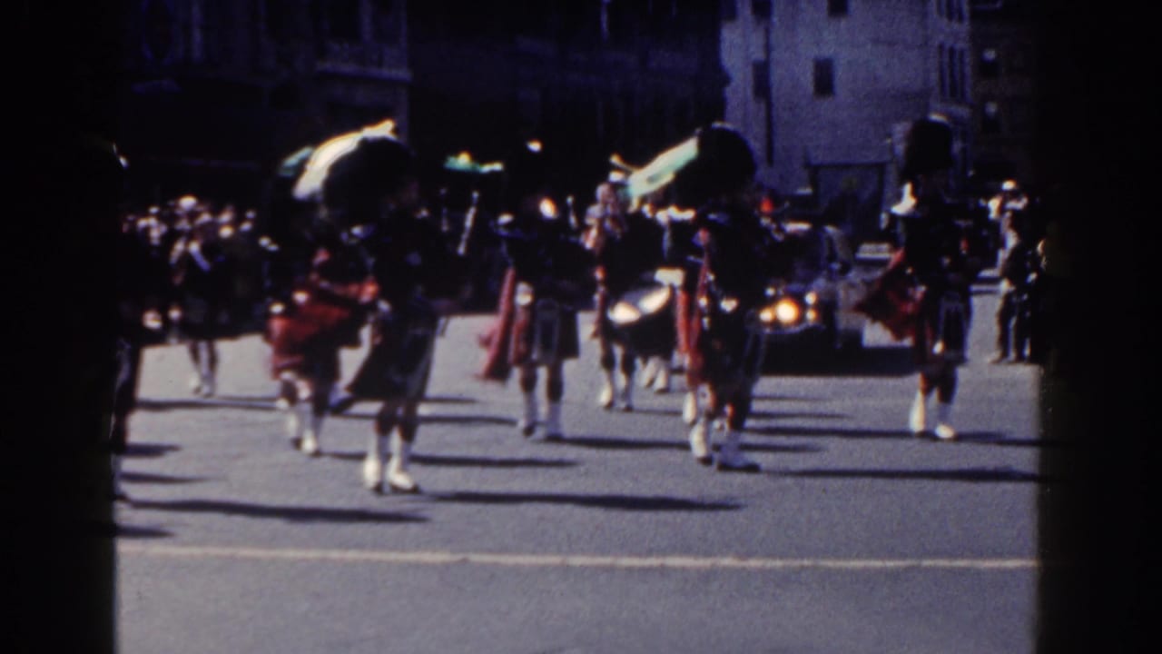 Kilted band members march along a city street during a parade.
