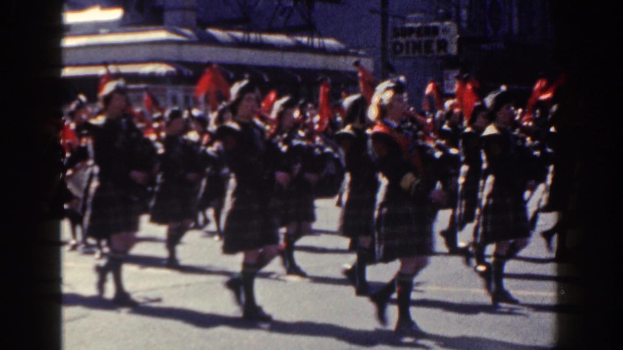 Closer view of uniformed band members carrying drums and instruments during a parade.