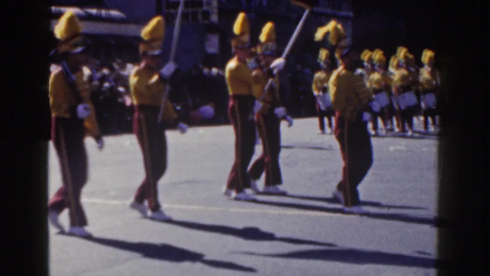 A New York City parade scene shows yellow-uniformed marchers and drummers moving in formation past a crowd, consistent with the 1962 clip metadata.