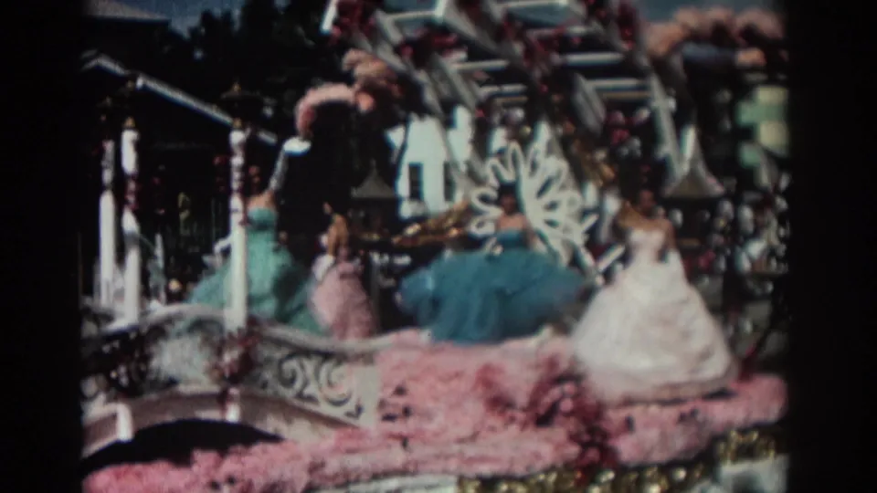 A closer 8mm view of the Pasadena float shows women in blue, pink, and white gowns framed by pink floral covering and ornate white-and-gold rail trim.