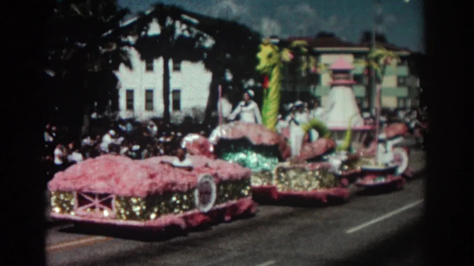 The Pasadena parade float shows a coiled green sea monster, pink trim, and riders in white uniforms waving from the float.