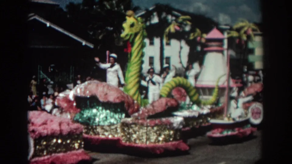 1962 Pasadena parade float with a green and yellow sea serpent, pink trim, and sailors in white uniforms waving from the float.
