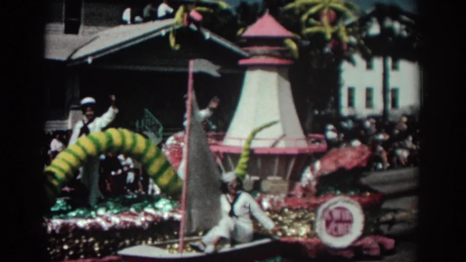 1962 Pasadena parade float detail showing sailors, a sailboat-shaped element, pink and gold trim, spectators, and a round side sign.
