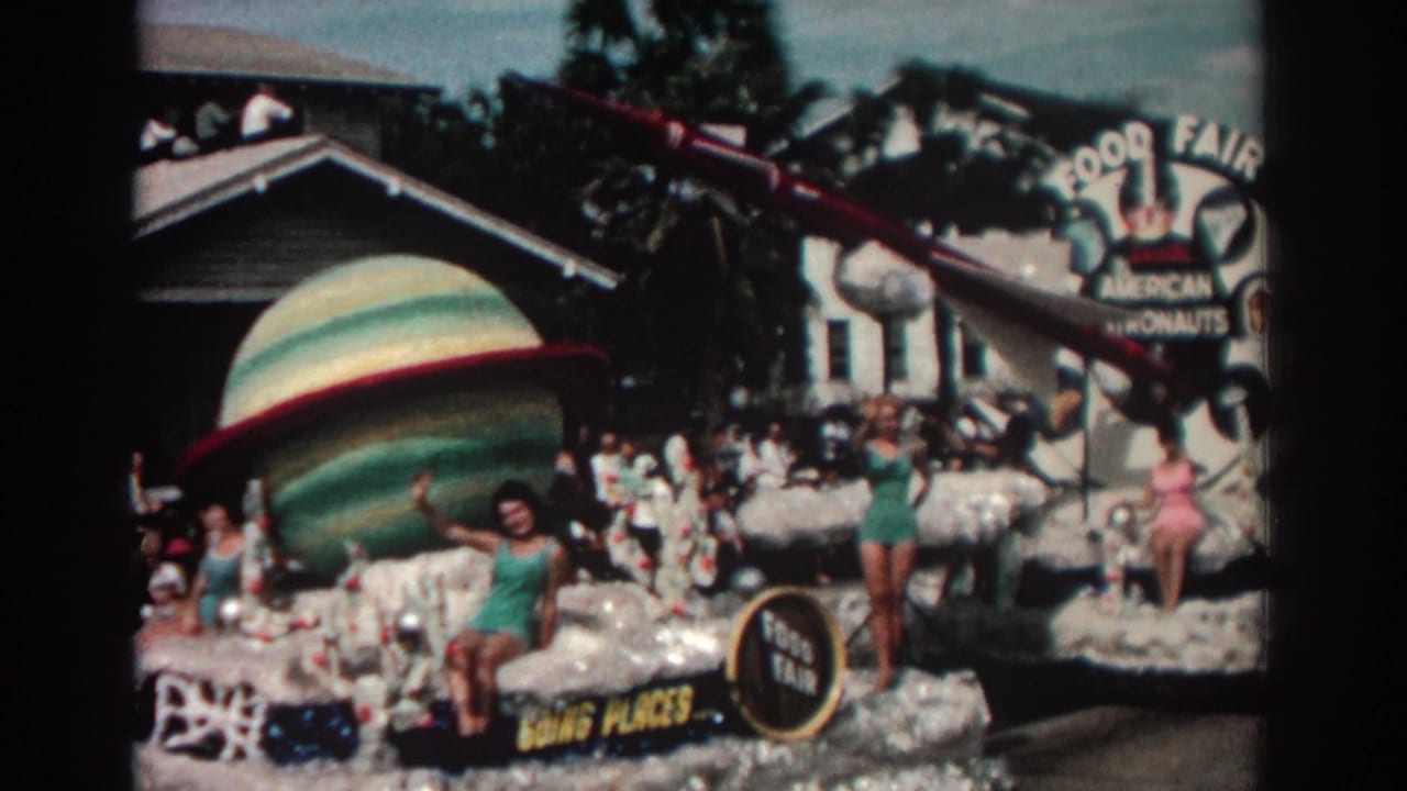 Space-themed parade float with women waving, a large planet prop, rocket, spectators, and Food Fair signage.