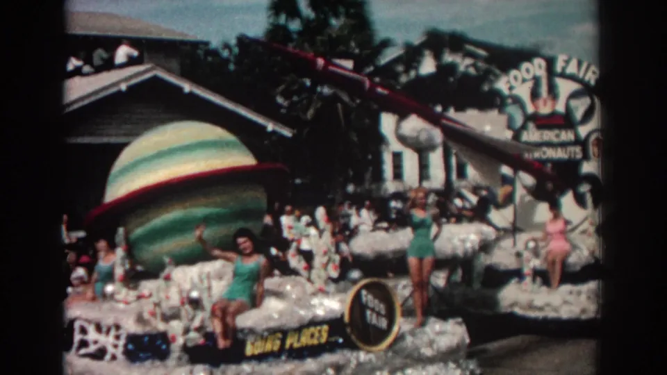 1962 Pasadena home-movie frame of a space-themed parade float with women waving beside a large planet and rocket prop.