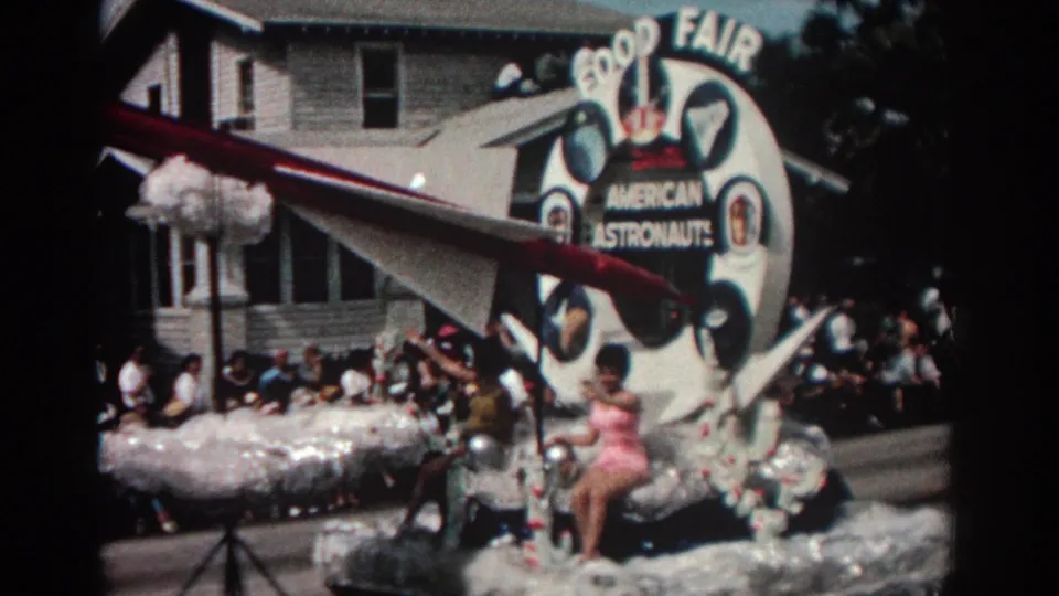 The Pasadena parade float carries a large astronaut display, red-and-white model rocket, and seated performer as crowds watch from the curb.