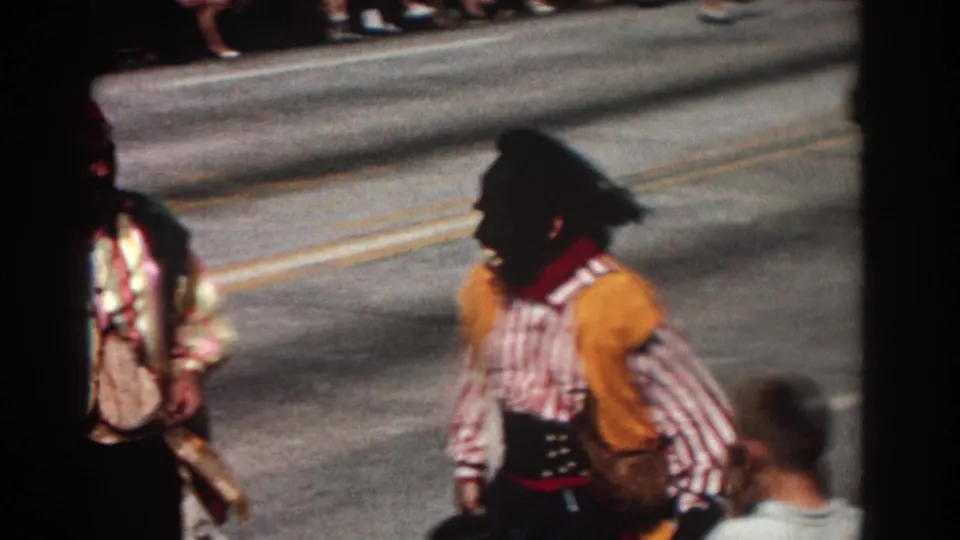 Later Pasadena parade frame showing a costumed marcher in blackface makeup walking along the street, requiring sensitive historical context.
