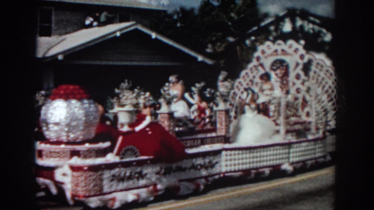 The Pasadena float advances with a large silver globe, red floral forms, white latticework, and women waving from the platform.