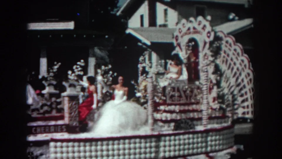 A Pasadena parade float passes close to camera, showing a woman in a white gown, a red-dressed rider, floral decorations, and CHICAGO CHERRIES lettering.