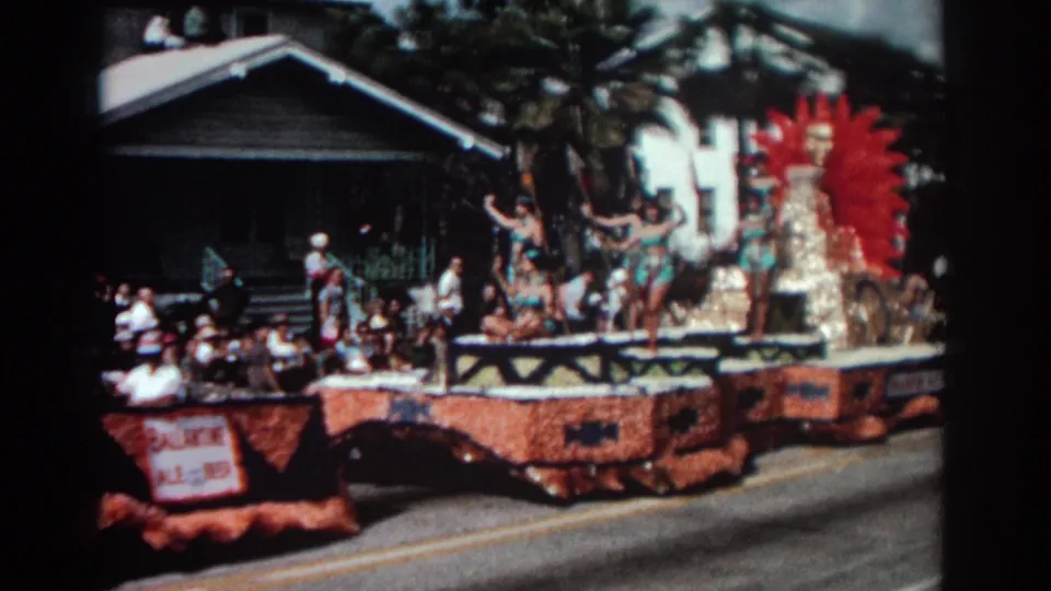 1962 Pasadena parade float with waving costumed performers, floral decoration, and spectators seated near houses.