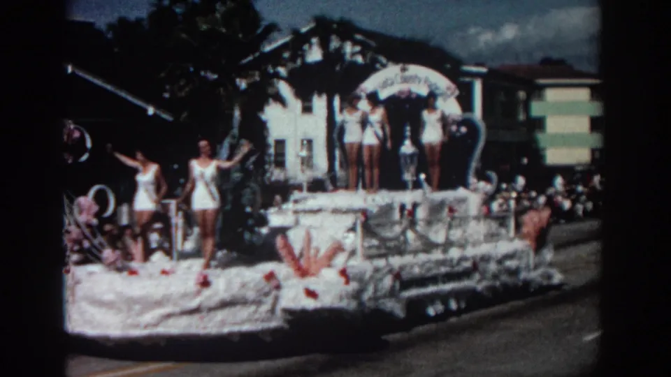 A closer 1962 Pasadena frame shows the float decorations, women in swimsuits, and the crowd lining the street behind the vehicle.