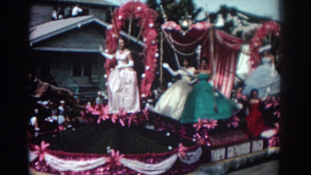 Four women in gowns wave from a pink and white decorated parade float.
