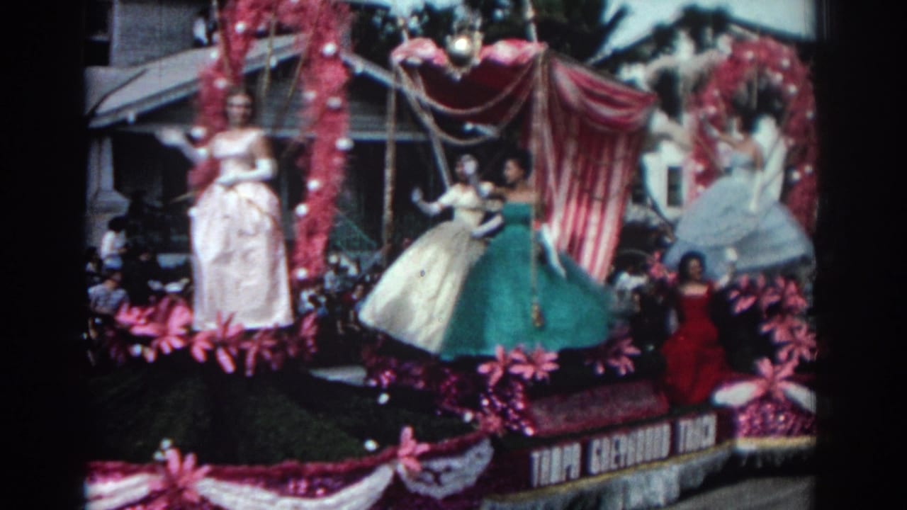 Decorated parade float with women in pastel gowns and spectators behind it.