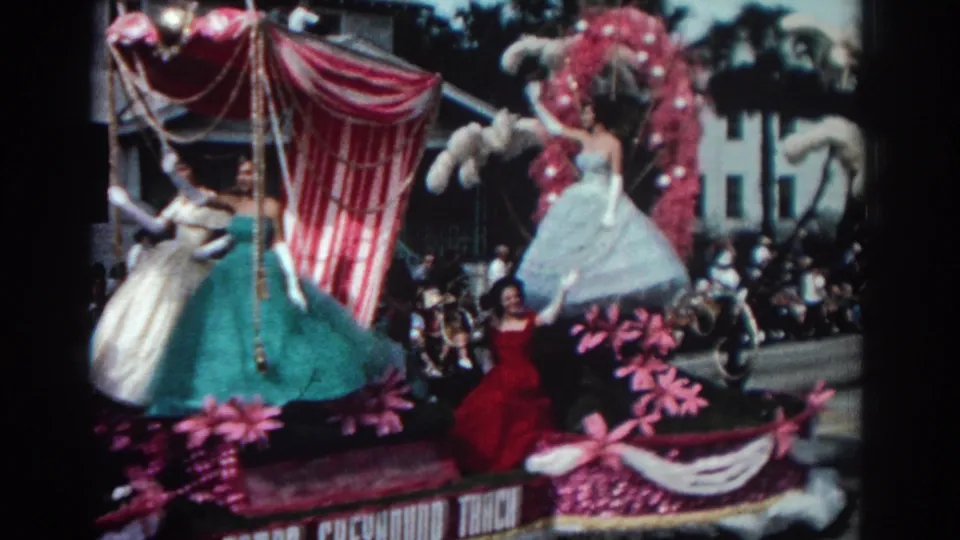 Final frame of the 1962 Pasadena parade clip, with women waving from a pink decorated float before street spectators.
