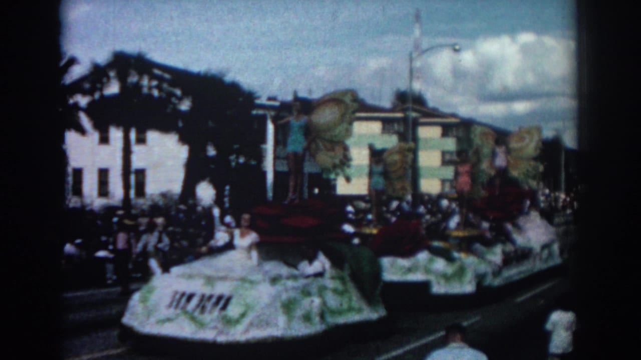 Parade float with large red roses, butterfly wings, women posing, and spectators along a Pasadena street.