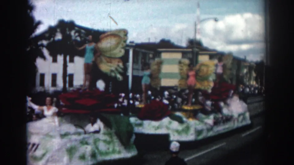 Closer 1962 Pasadena parade view with women posed on a floral float, large butterfly wings, red rose decorations, and crowds along the curb.