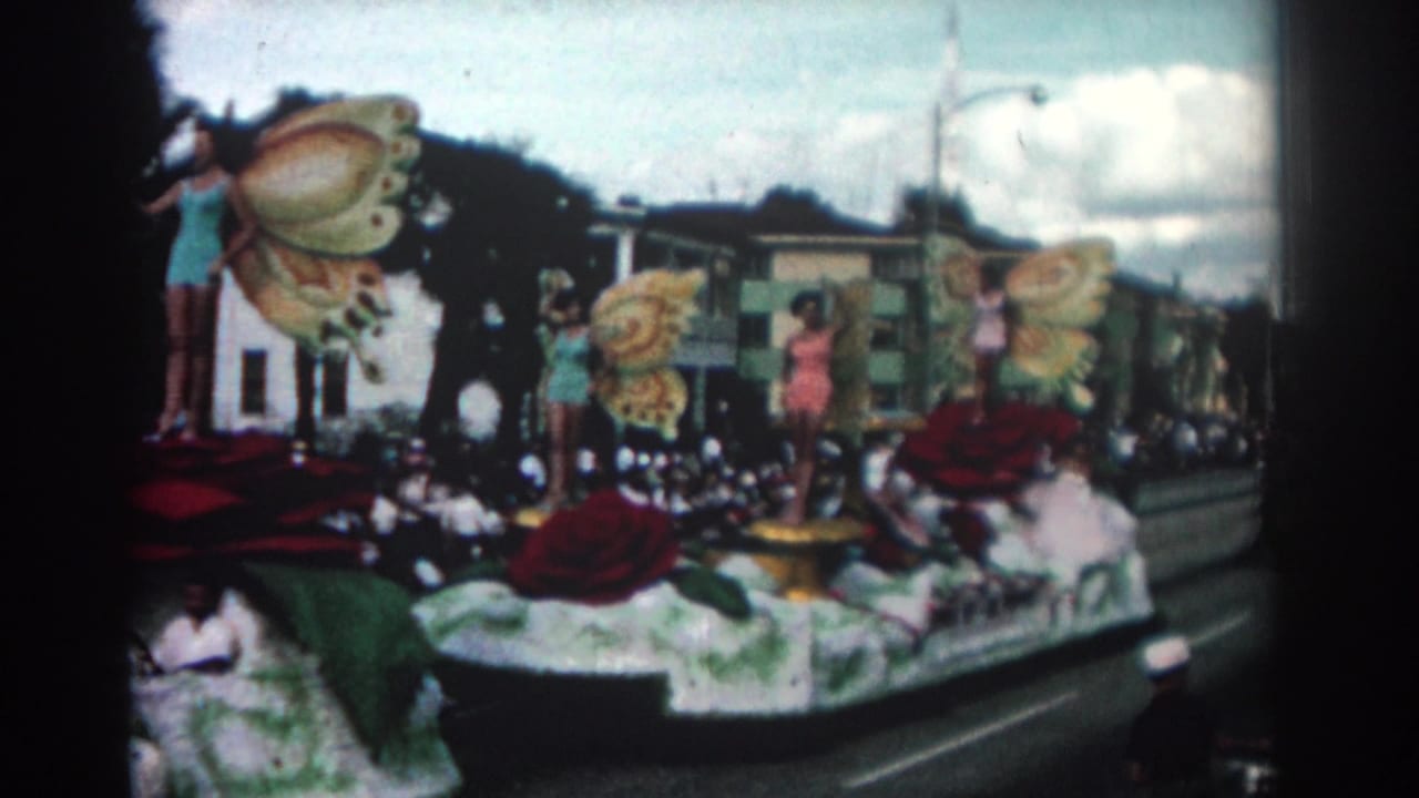 Decorated parade float with women in butterfly costumes passing spectators on a city street.