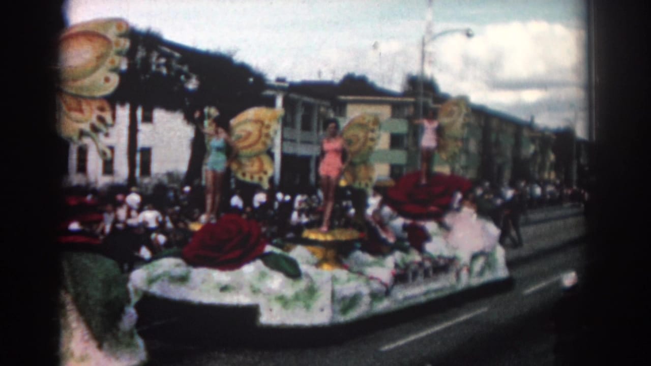 Parade float with butterfly decorations and costumed women viewed from the roadside.