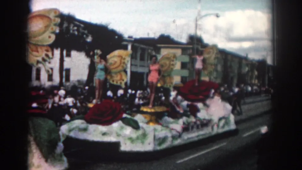 Roadside 8mm view of a Pasadena parade float with oversized butterfly wings, red floral forms, and spectators behind it.