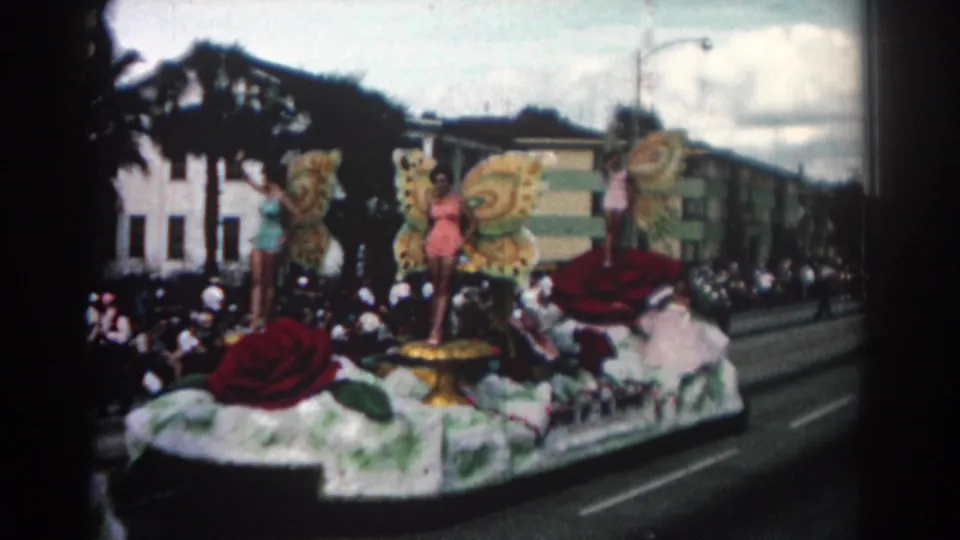 1962 Pasadena parade scene showing a decorated float with large roses, butterfly-wing figures, and spectators along the curb.