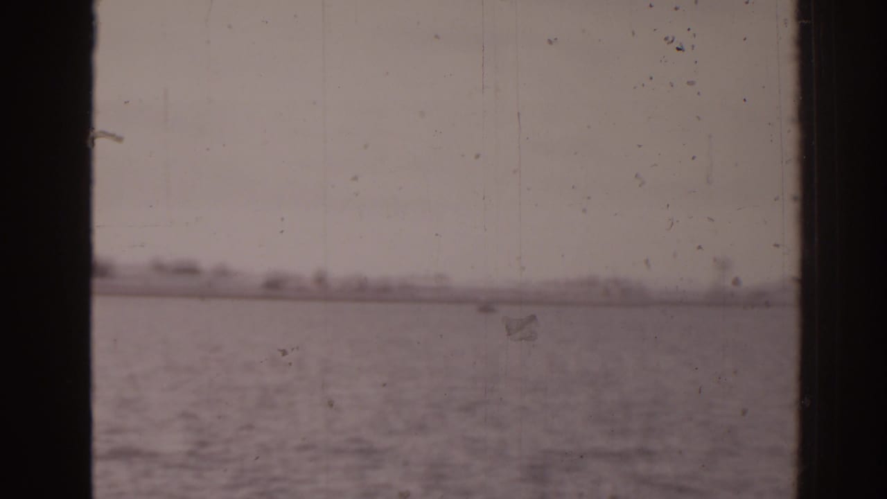 1963 Florida 8mm view of calm sea and a hazy distant shoreline framed by dark boat-window edges.