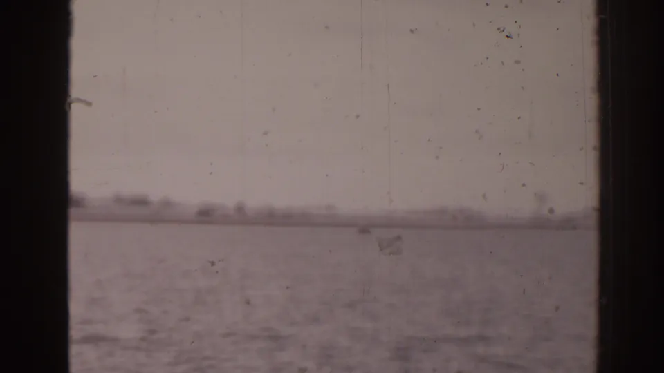 1963 Florida 8mm view of calm sea and a hazy distant shoreline framed by dark boat-window edges.