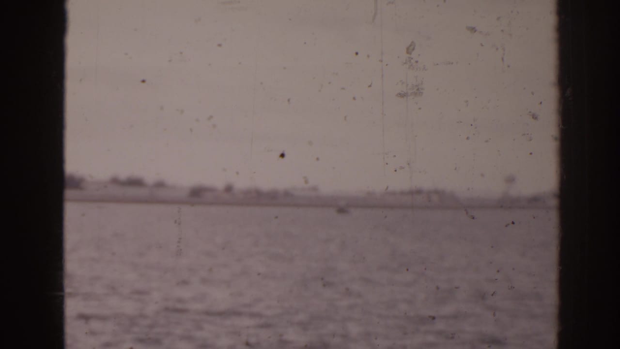 Soft 8mm Florida coastal view showing open water, pale sky, and low distant land from a moving boat.