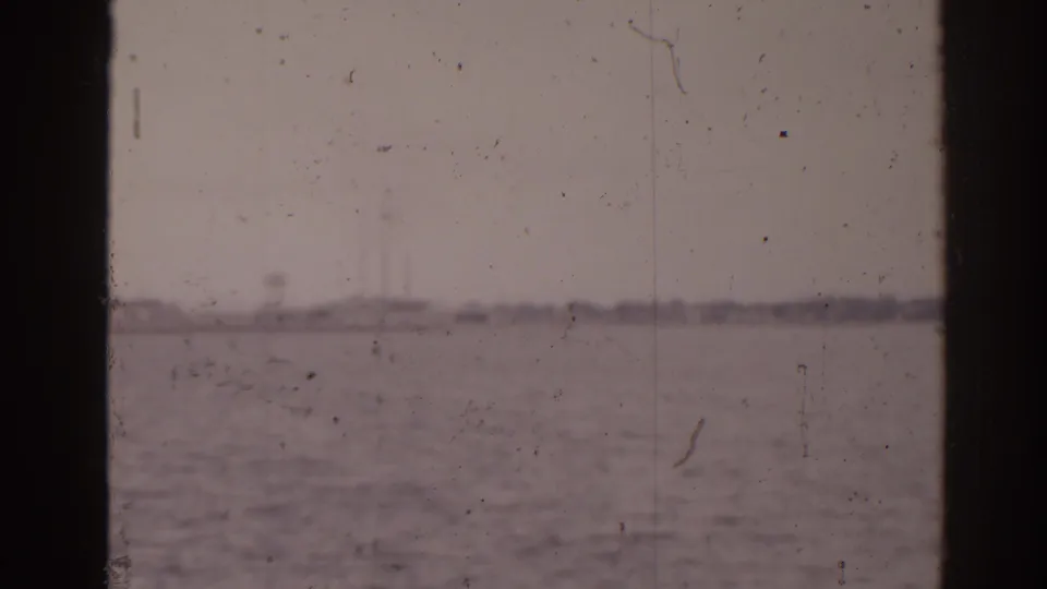 1963 home-movie frame of Florida water and far shoreline, filmed through or past dark boat-window edges.