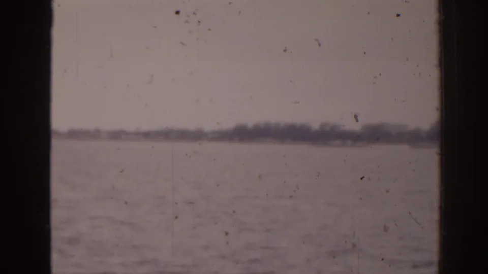 1963 Florida home-movie frame with muted water, overcast sky, and indistinct shoreline seen through dark vertical framing.