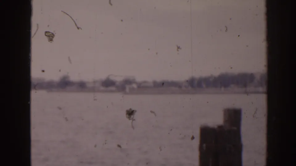 1963 Florida 8mm frame showing calm water, a hazy shoreline, and a wooden pier post entering the lower foreground.