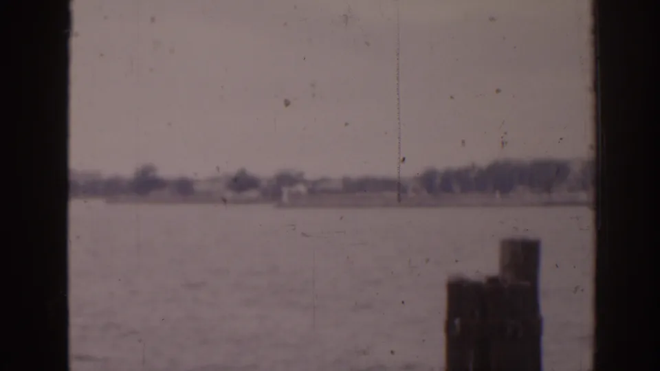 1963 Florida waterfront frame with a dark pier post in the foreground and a hazy shore across the water.