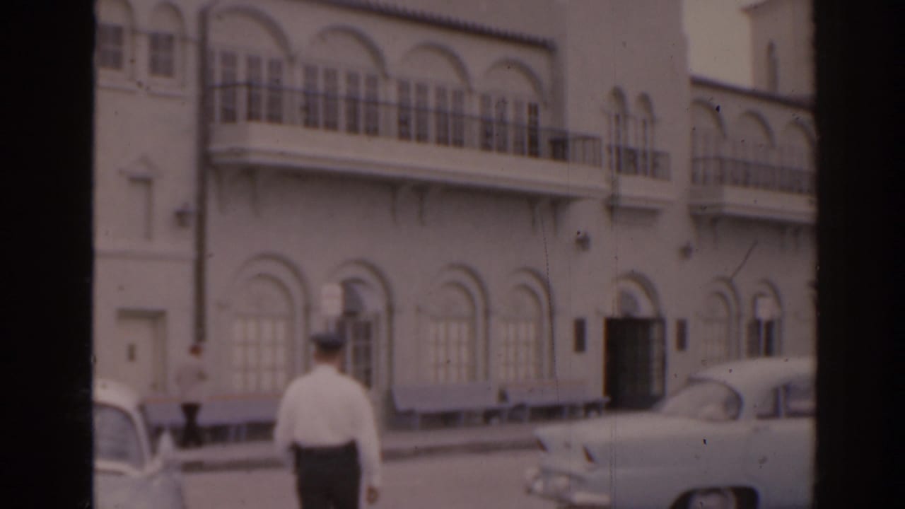 Man walking past parked cars outside a white arched building.