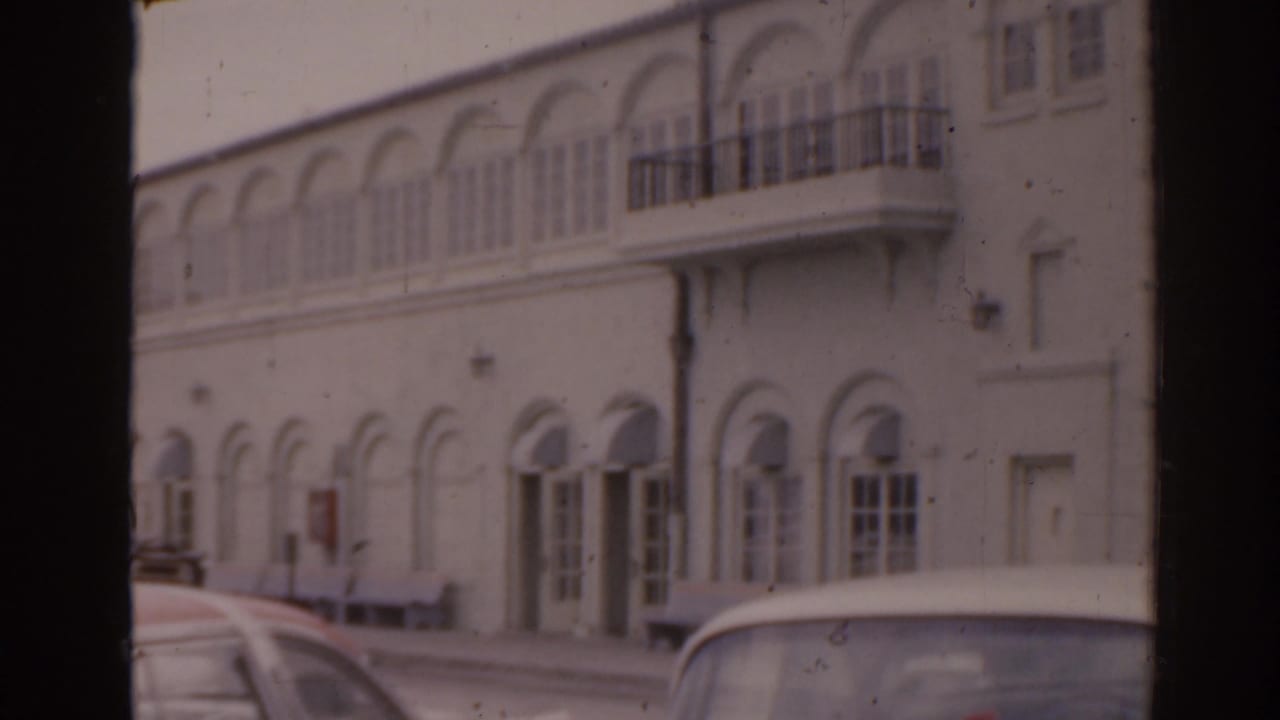 Parked cars beside a white building with arched doors and balconies.