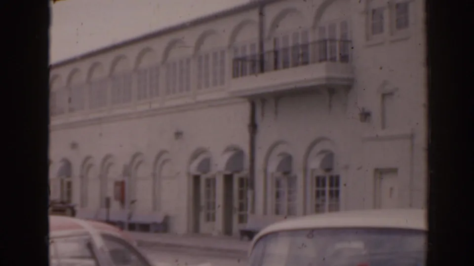 1963 Florida coastal street view with classic cars parked by a white arched building, seen through a dark frame.