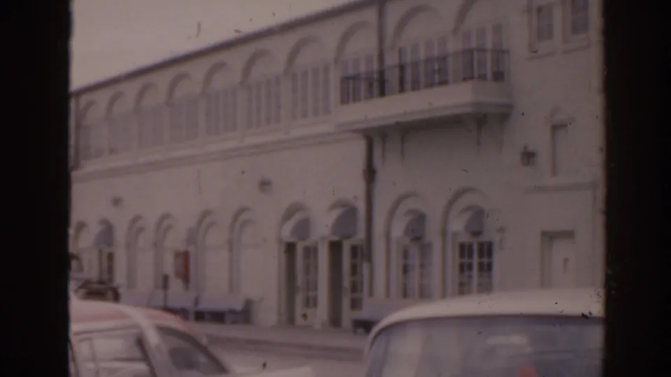 Soft 8mm view of a Florida building with arched windows, balconies, and parked 1960s cars along the street.