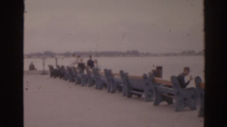 1963 Florida waterfront scene with benches, seated people, open pavement, and a hazy view across the water.