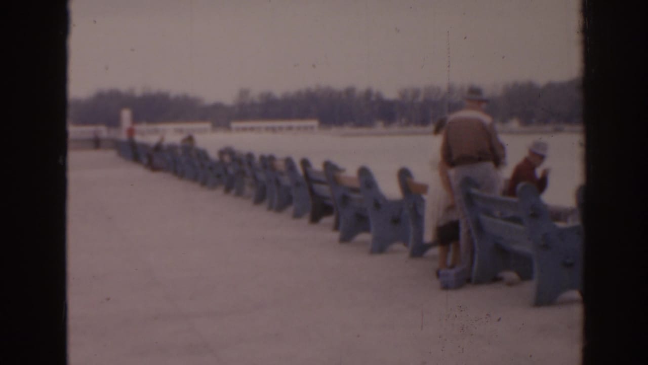 Waterfront walkway with blue railings or benches and two adults near the edge.