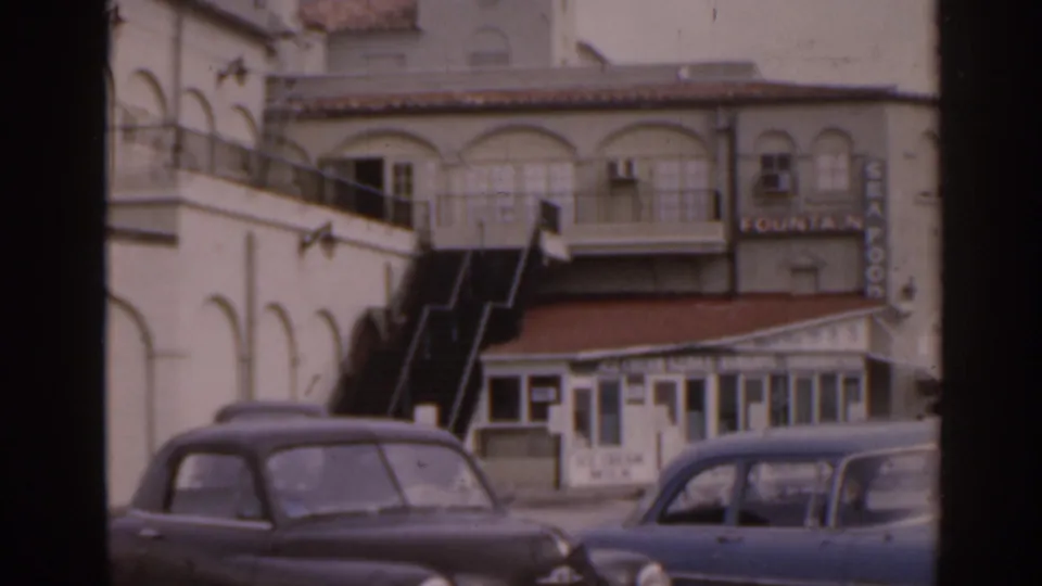 1963 Florida street view of a white stucco building with arched details, exterior stairs, parked cars, and a readable Fountain sign.