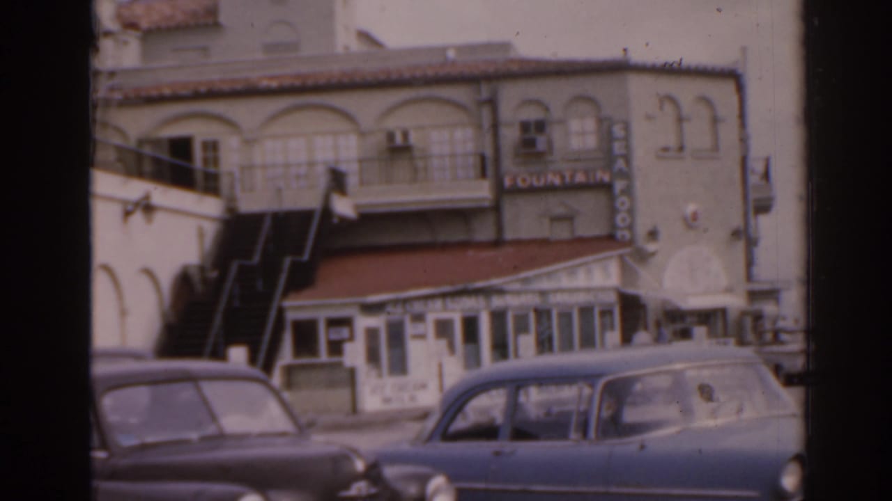 Streetfront building with Fountain sign, storefront windows, stairs, and parked cars.