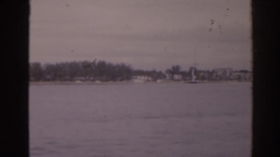 1963 Florida 8mm waterfront view across calm water toward trees and low buildings on a distant shore.