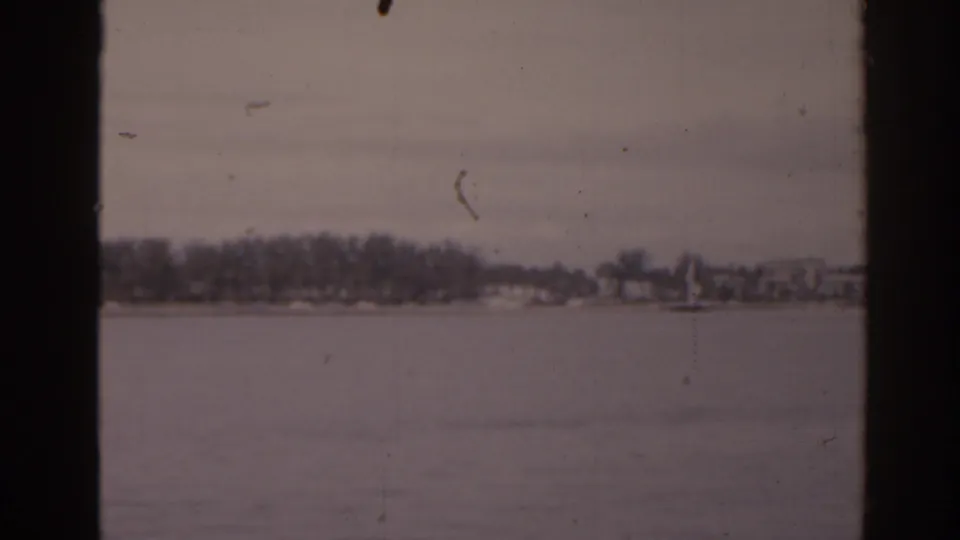 1963 Florida 8mm view across a calm lake toward a distant shoreline with trees and low buildings.
