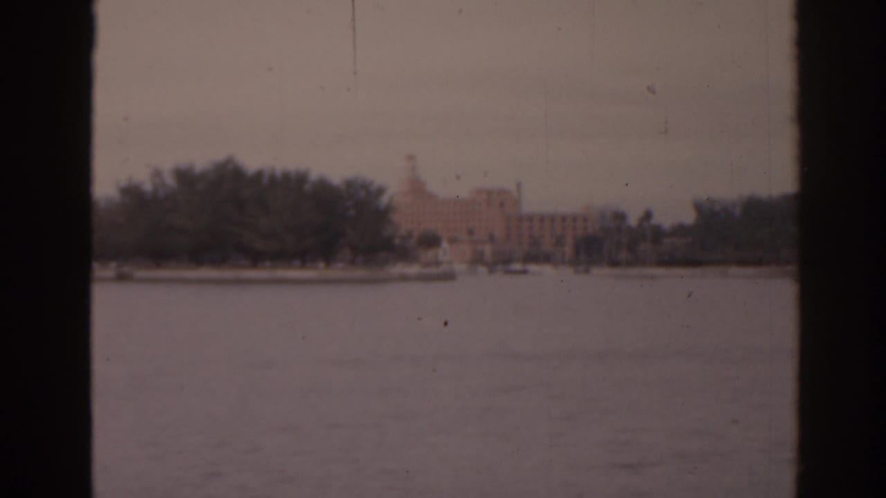 Distant pale waterfront building with tower across water, framed by dark vertical edges.
